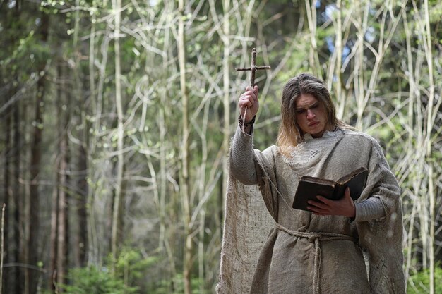 A man in a cassock spends a ritual in a dark forest with a crystal ball and book