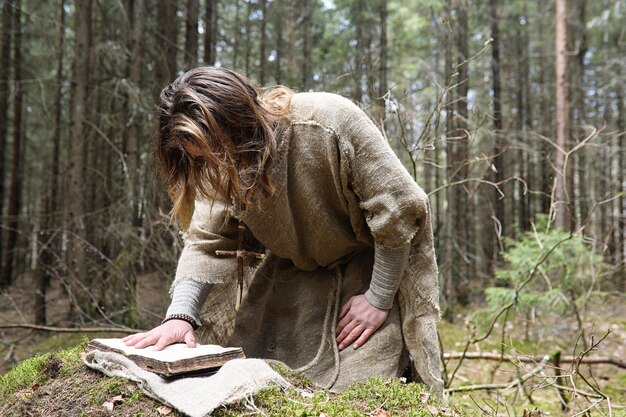 Foto un uomo in cassotta trascorre un rituale in una foresta buia con una palla di cristallo e un libro