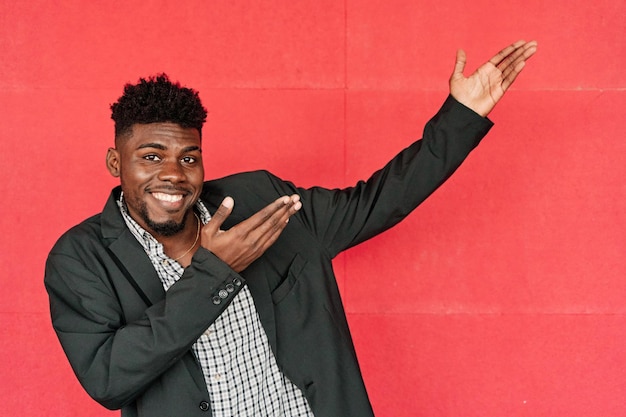 Man in casual blazer points to copy space on red background young africanamerican man smiling