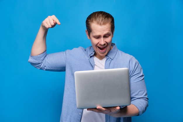 Photo man in casual clothes on blue is about to press button in laptop with smile.