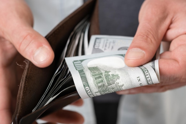 A man in casual clothes holds a male wallet with money and hundred dollar bills in his hands