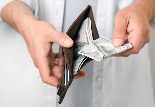 Un uomo in abiti casual tiene in mano un portafoglio maschile con denaro e banconote da cento dollari