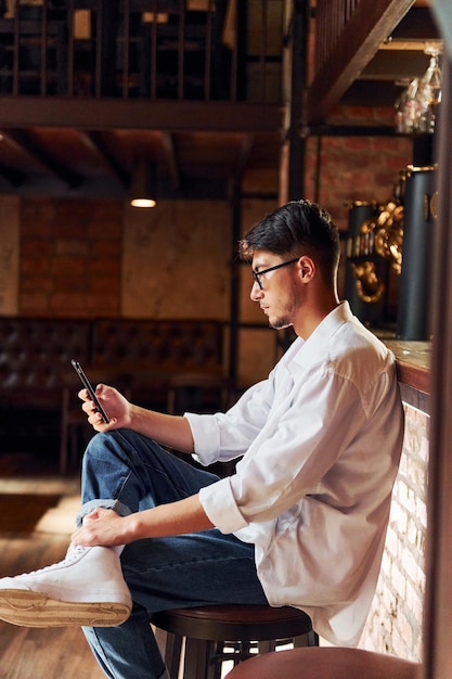 Man in casual clothes sitting in the pub with phone in hand