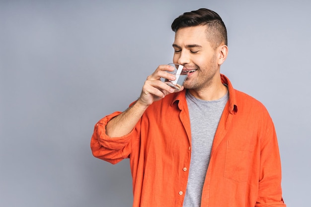 A man in casual isolated over white grey background drinking water from a glass Thumbs up