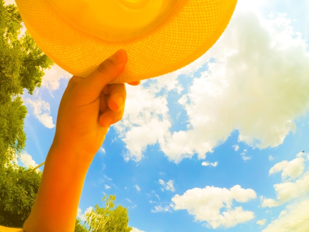 A man of Caucasian race holds a hat in his hand. On the background of sky and white clouds. Abstract concept of summer vacation holiday. Bottom view.