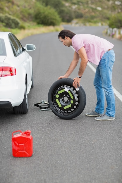 Человек меняет колесо после пробоя автомобиля