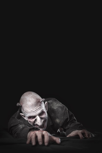 Man characterized as a zombie crawling on the floor. Black background.