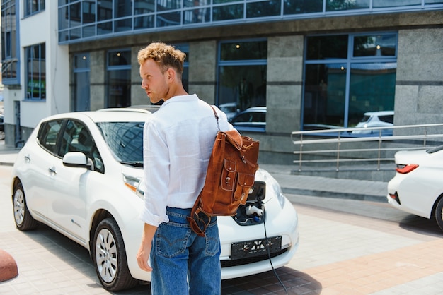 Man charging his luxury electric car at outdoor station in front of modern new city buildings