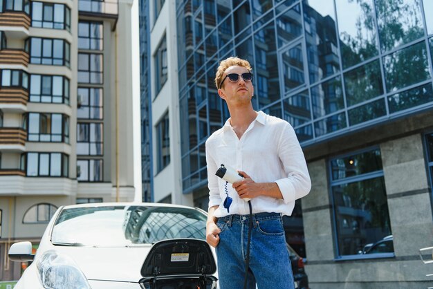 Man charging his luxury electric car at outdoor station in front of modern new city buildings