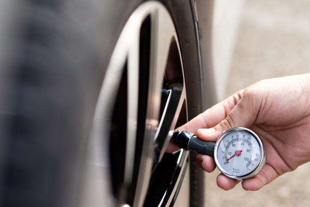 Man checking his car tire with tire pressure gauge