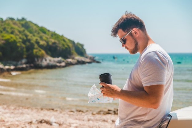 Man checking on map at car hood destination place sea beach on background summer time