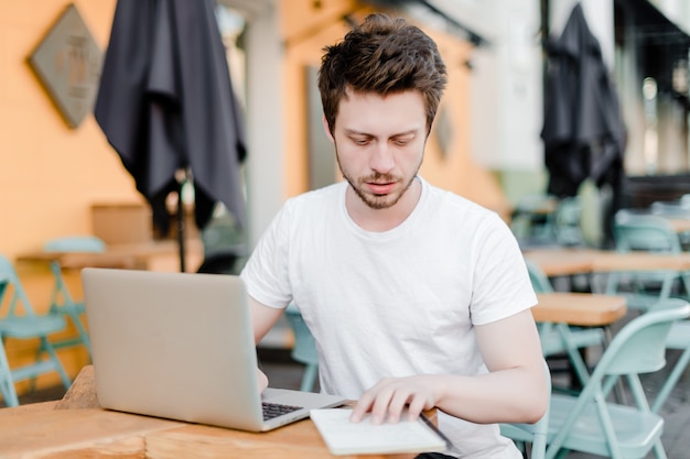 Uomo che controlla taccuino e computer portatile concentrati all'aperto