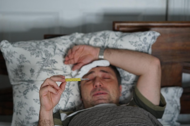 Man checking temperature while lying on bed at home