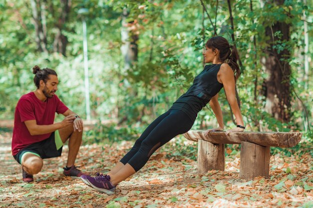 Man checking time while friend exercising on wooden bench in forest