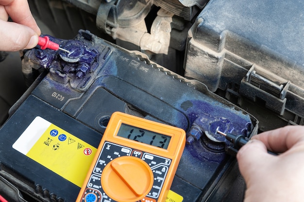 Man checks car battery by using a digital multimeter with\
voltage range measurement