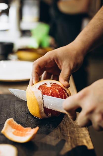 Man chef cutting grapefruit at the kitchen restaurant