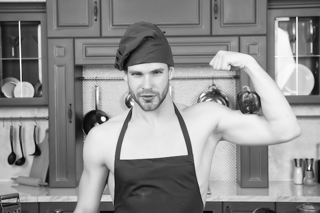 Man in chef hat apron on sexy torso flex hand muscles with red pepper in kitchen Vegetarian healthy food diet concept Energy power health fitness sport Cooking culinary cuisine