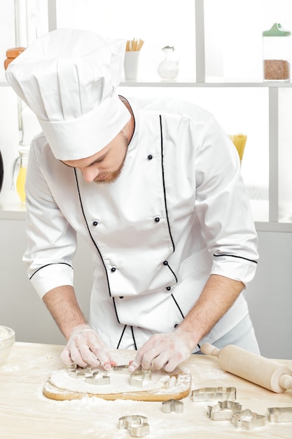 Man chef-kok in uniform maakt koekjes met bakvormen