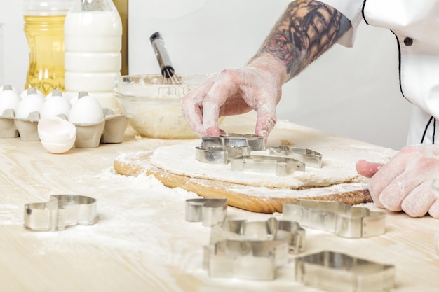 Man chef-kok in uniform maakt koekjes met bakvormen