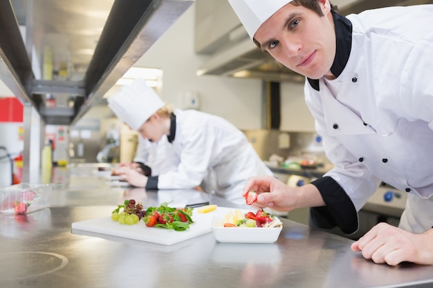 Photo man chef putting a strawberry in fruit salad