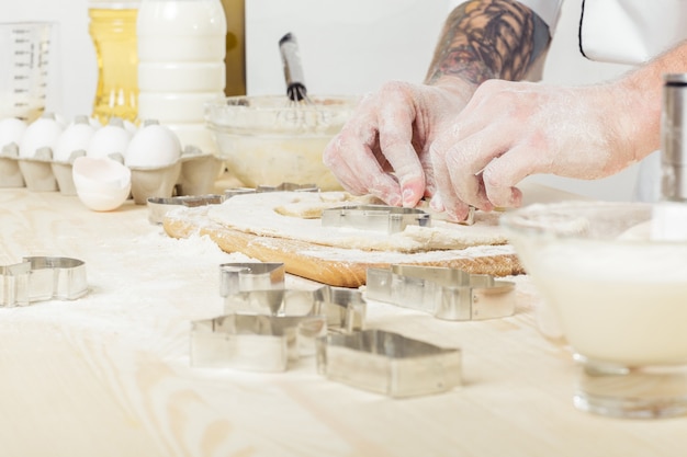 Man chef in the uniform makes cookies with baking forms