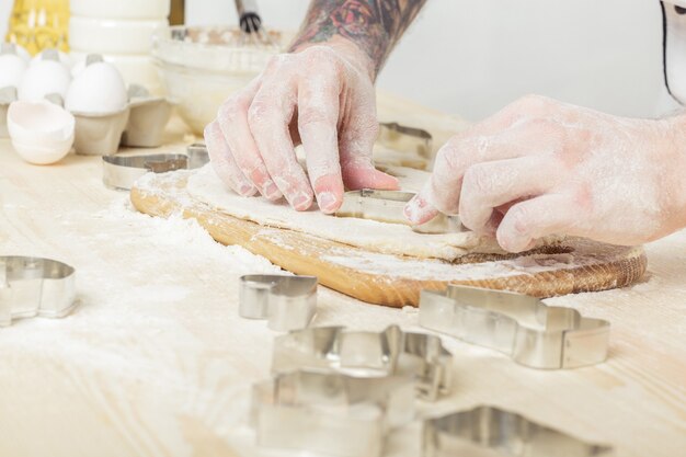 Man chef in the uniform makes cookies with baking forms