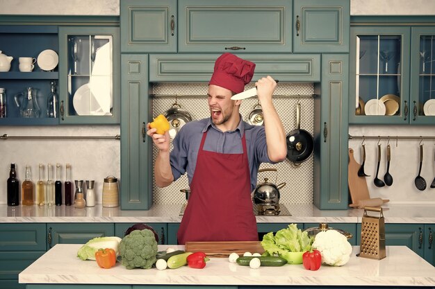 Man chef with angry face with knife cut pepper