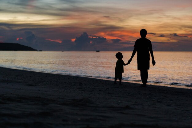 男と子供が夕暮れの浜辺を歩く。