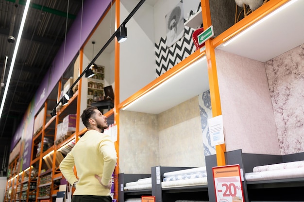 Photo a man chooses finishing materials for repairs in his house next to the racks in a construction hypermarket