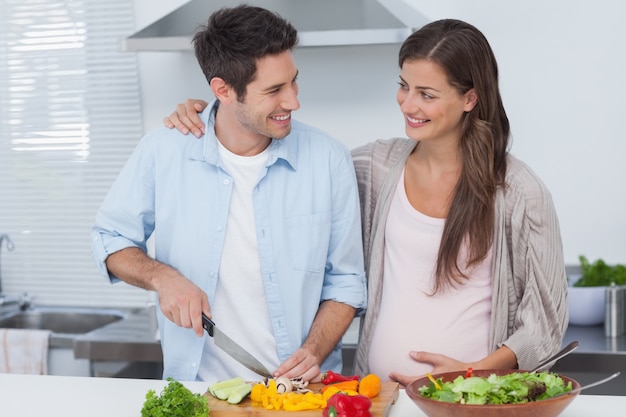 Человек, измельчая овощи рядом со своим беременным партнером