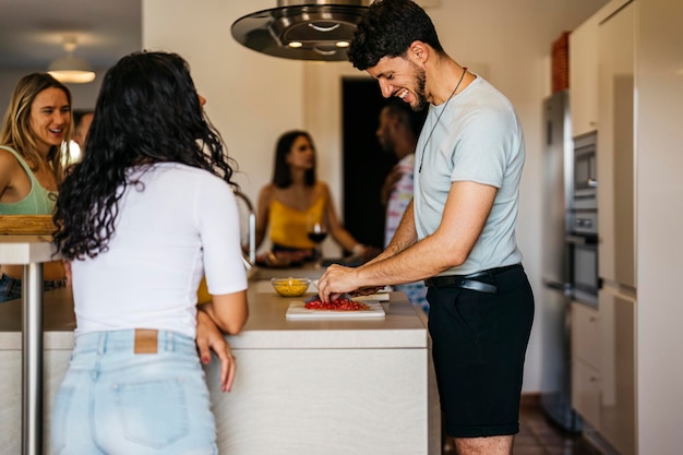 A man chops tomatoes with several friends having fun in the kitchen