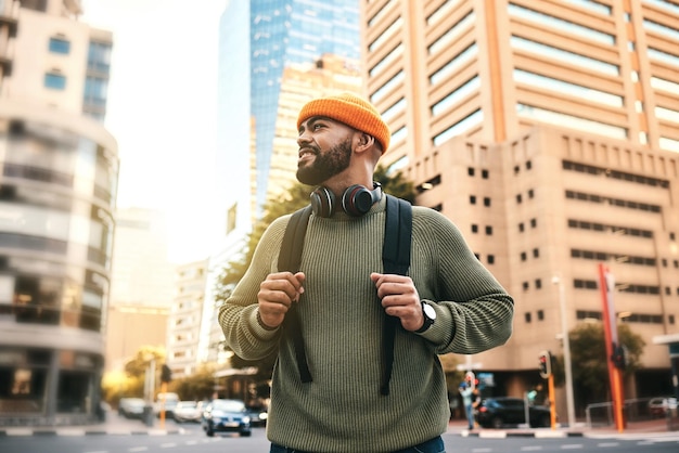 Foto uomo in città zaino e sorriso durante il tragitto mattutino verso il campus universitario per l'istruzione con edifici opportunità di studio e felice studente universitario gen z che cammina per strada urbana e si reca a scuola