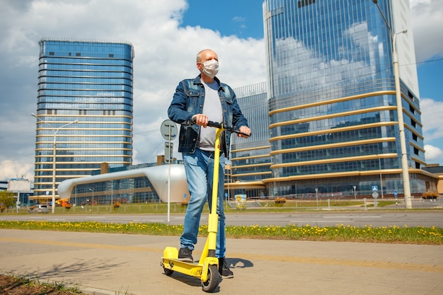 コロナウイルスを保護するための保護マスクの電動スクーターで街の通りにいる男。