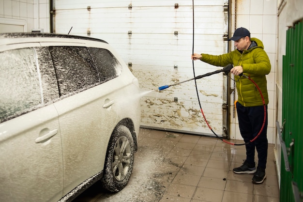 Man cleaning automobile with high pressure water at car wash.