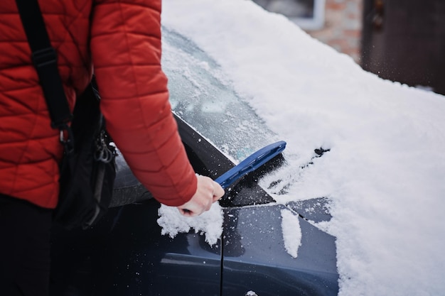 Uomo che pulisce l'auto da neve e ghiaccio con spazzola e raschietto durante l'emergenza invernale di nevicate