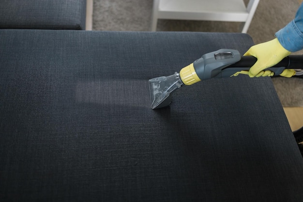 Man cleaning couch with washing vacuum cleaner closeup