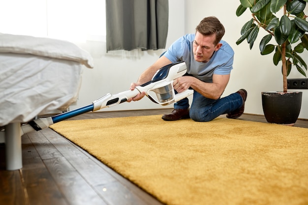 モダンな白いリビング ルームの掃除機で床を掃除する男性は、現代の新しい掃除機で簡単に掃除できるというコンセプト