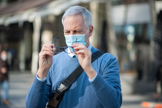 Man cleaning his eyeglasses fogged due to the mask covid coronavirus vision concept