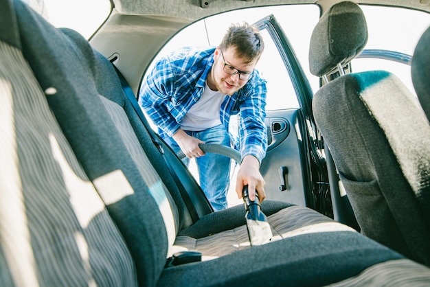 Man cleaning inside car with vacuum cleaner carwash concept