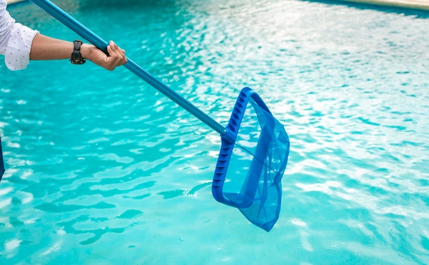 Un uomo che pulisce la piscina con lo skimmer a foglie uomo che pulisce la piscina con lo skimmer persona con lo skimmer che pulisce la piscina mani che tengono uno skimmer con piscina blu sullo sfondo