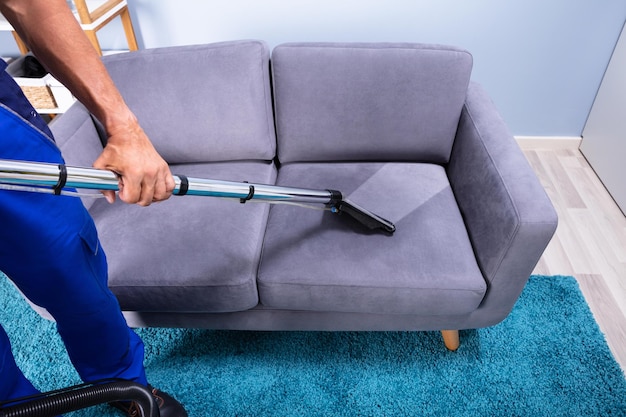 Man cleaning sofa with vacuum cleaner