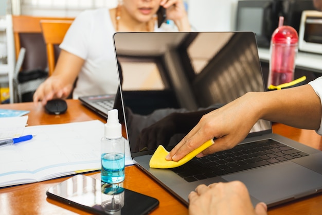 Man cleaning surface of keyboard laptop with yellow microfiber cloth with liquid alcohol sanitizer .