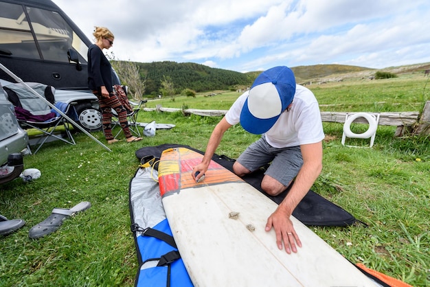 man cleaning surfboard on grassy land