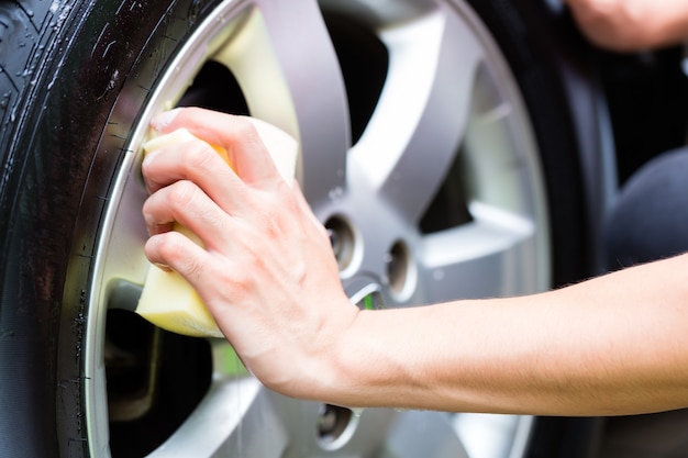 man cleaning wheel rim while car wash