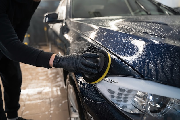 Человек чистит кузов автомобиля круговой губкой.