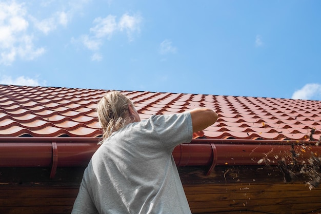 A man cleans the gutter of a drainpipe from dry leaves and debris Prevention of congestion and breakage of the gutter drain