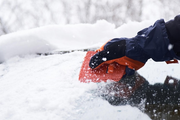 降雪後に車を掃除する男性 フロントガラスの雪を掃除する 氷をかき集める 冬の車の窓掃除