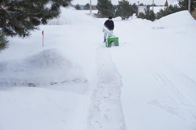 A man cleans snow in the winter in the courtyard of the house man cleaning snow with a snow blower