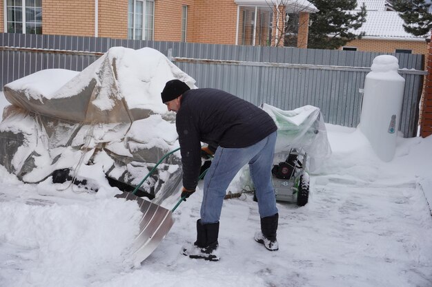 A man cleans snow in the winter in the courtyard of the house