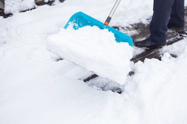 A man cleans the snow with a big blue shovel.